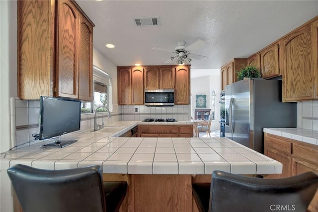 kitchen with tile counters, kitchen peninsula, sink, and appliances with stainless steel finishes