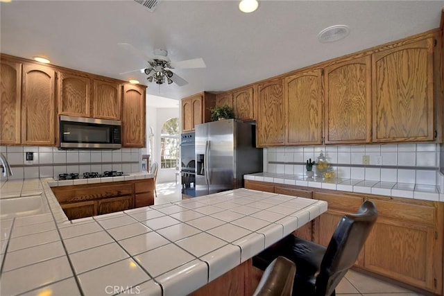 kitchen featuring tile countertops, sink, decorative backsplash, ceiling fan, and stainless steel appliances