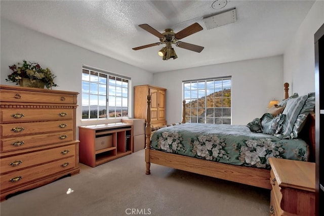 carpeted bedroom featuring multiple windows, ceiling fan, and a textured ceiling