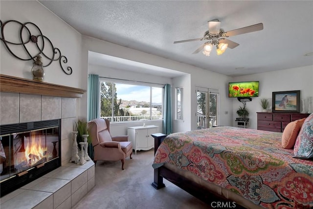 bedroom with ceiling fan, access to exterior, a fireplace, a textured ceiling, and light colored carpet