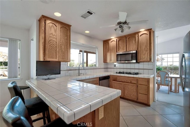 kitchen featuring tile counters, sink, tasteful backsplash, kitchen peninsula, and appliances with stainless steel finishes