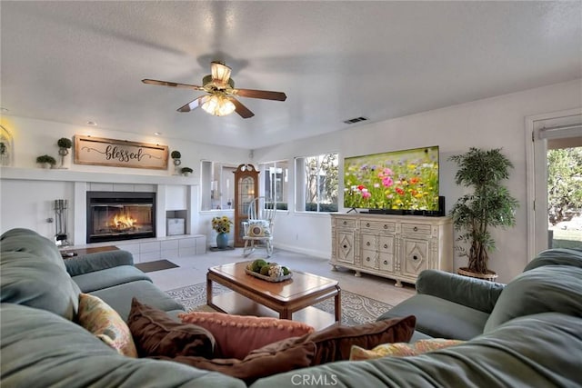 living room with a tile fireplace, ceiling fan, and a textured ceiling