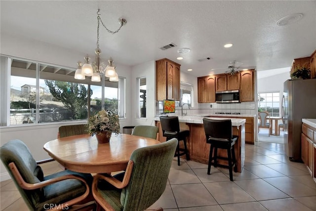 tiled dining space with a textured ceiling, ceiling fan with notable chandelier, and sink