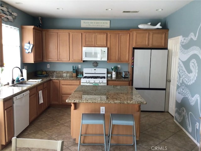 kitchen featuring light stone countertops, white appliances, sink, a center island, and a breakfast bar area