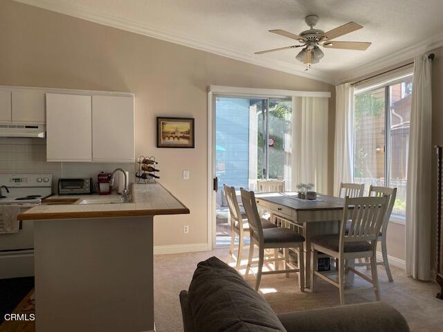 dining space with ceiling fan, sink, lofted ceiling, light carpet, and ornamental molding