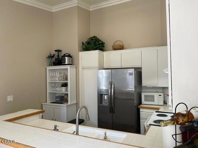 kitchen featuring tile counters, kitchen peninsula, crown molding, white appliances, and white cabinets