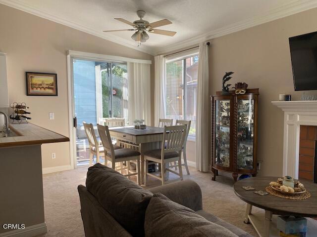 carpeted dining area featuring a tile fireplace, vaulted ceiling, ceiling fan, and crown molding