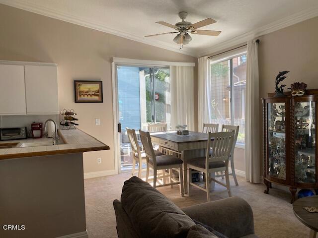 dining room featuring ceiling fan, sink, light colored carpet, lofted ceiling, and ornamental molding