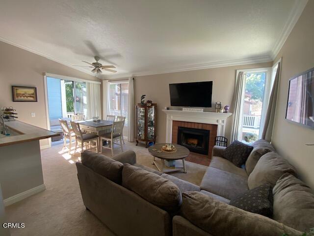 carpeted living room with a tiled fireplace, crown molding, and ceiling fan