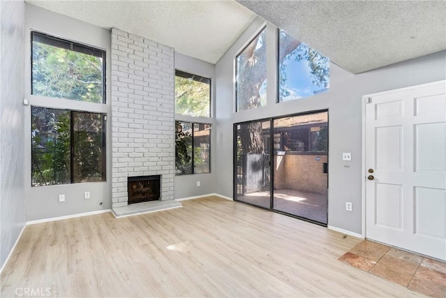 unfurnished living room with a textured ceiling, light wood-type flooring, and a brick fireplace