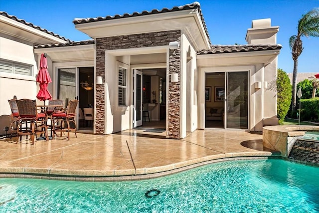 rear view of house featuring a swimming pool with hot tub and a patio