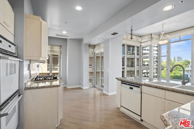 kitchen with dark stone counters, white appliances, sink, pendant lighting, and light hardwood / wood-style floors