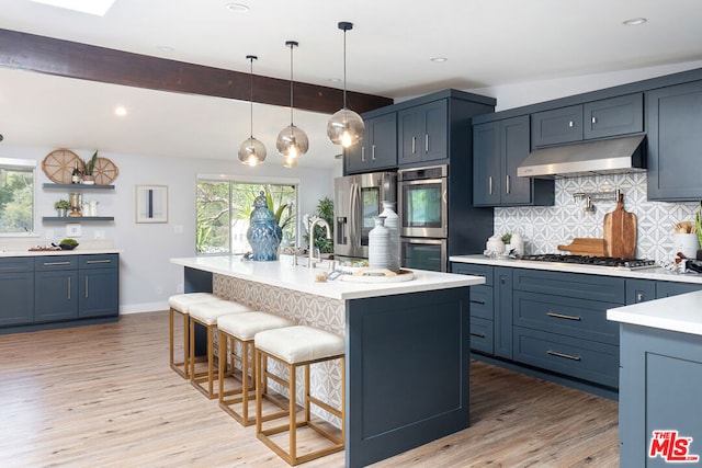 kitchen with a kitchen island with sink, a breakfast bar area, light hardwood / wood-style flooring, decorative backsplash, and stainless steel appliances