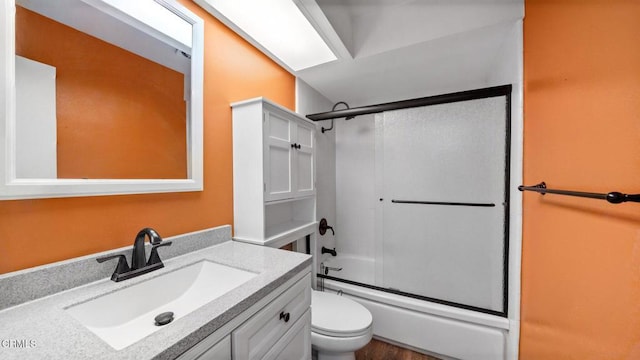 full bathroom featuring shower / bath combination with glass door, hardwood / wood-style floors, vanity, and toilet