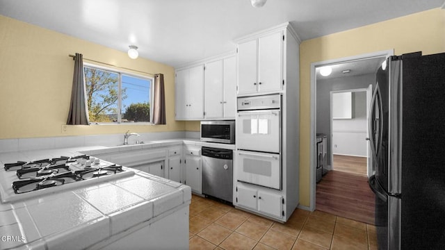 kitchen with tile counters, sink, stainless steel appliances, white cabinets, and light tile patterned flooring