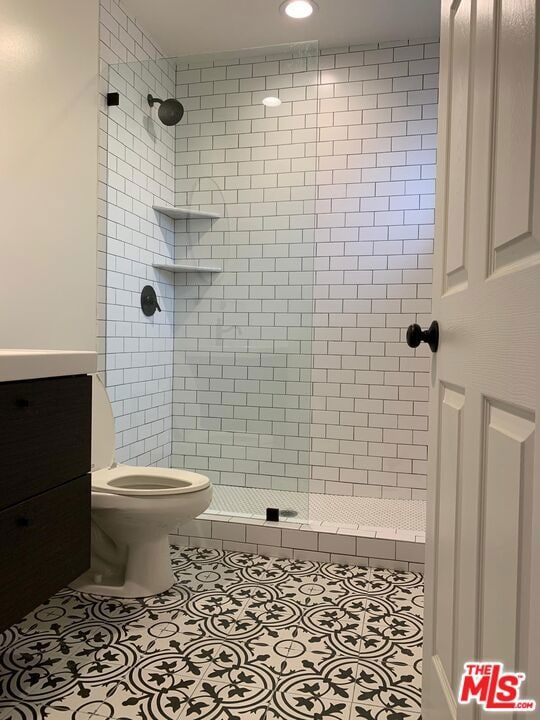 bathroom featuring tiled shower, tile patterned flooring, vanity, and toilet