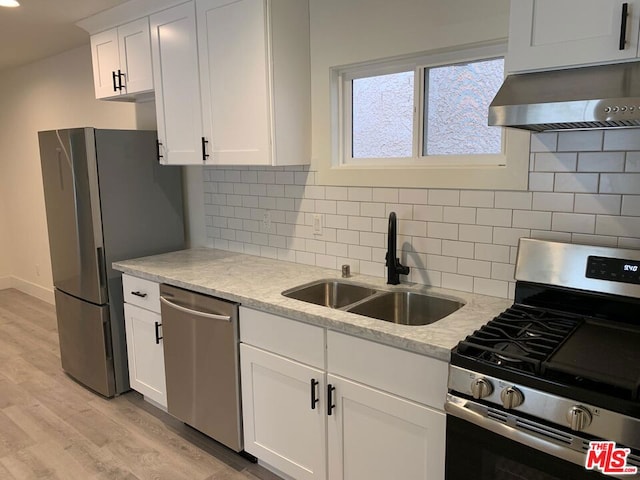 kitchen with stainless steel appliances, wall chimney range hood, sink, white cabinets, and light hardwood / wood-style floors