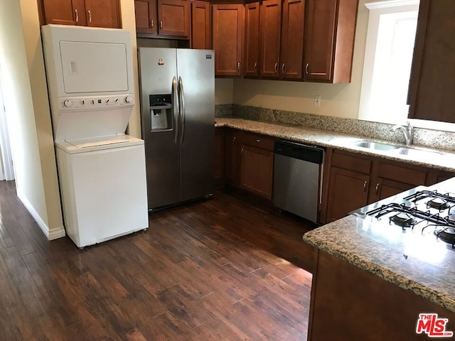 kitchen featuring appliances with stainless steel finishes, dark hardwood / wood-style flooring, stacked washer and clothes dryer, and sink