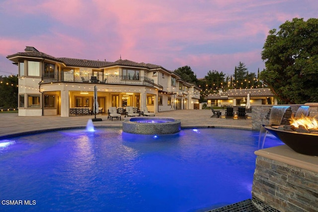 pool at dusk with a patio area, pool water feature, an in ground hot tub, and an outdoor fire pit