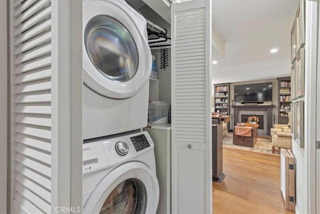 laundry area featuring radiator heating unit, light hardwood / wood-style floors, and stacked washer / drying machine