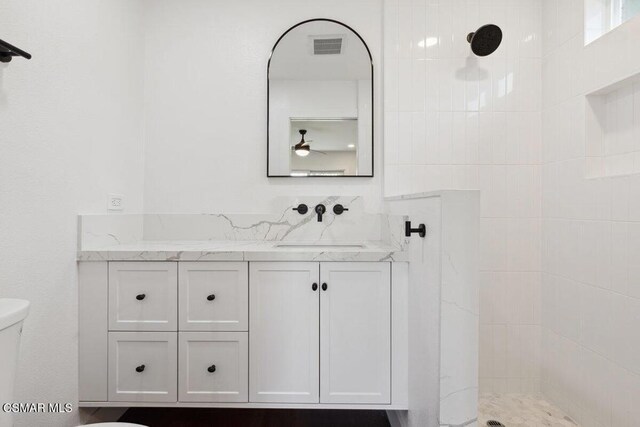 bathroom featuring a tile shower, vanity, and toilet