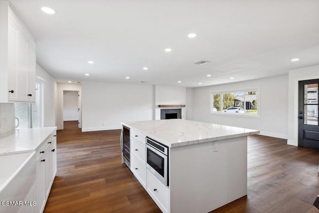 kitchen with white cabinets, dark hardwood / wood-style flooring, a kitchen island, and stainless steel microwave