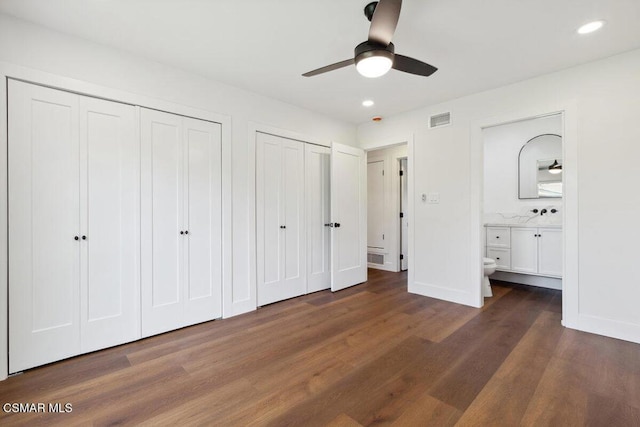 unfurnished bedroom featuring ensuite bath, ceiling fan, dark wood-type flooring, and two closets