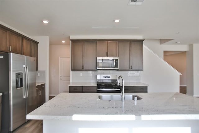 kitchen featuring dark brown cabinetry, stainless steel appliances, light stone counters, and sink