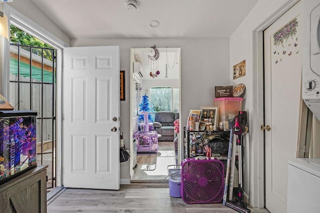 foyer entrance with light wood-type flooring, stacked washer and dryer, and a wall unit AC