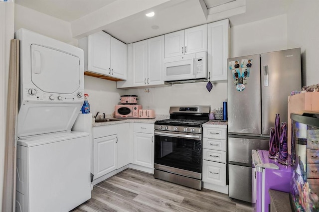 kitchen with sink, stainless steel appliances, light hardwood / wood-style flooring, white cabinets, and stacked washer and clothes dryer