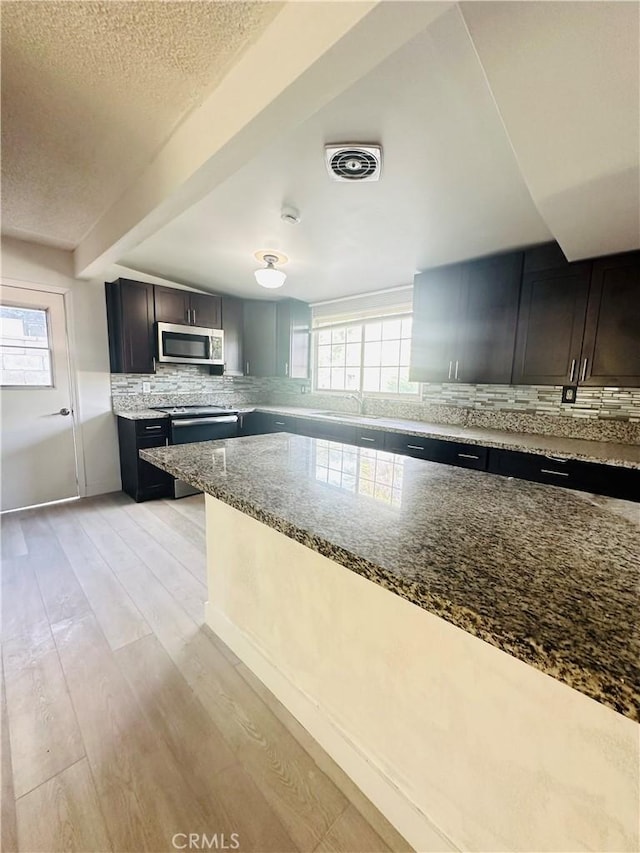 kitchen with backsplash, dark brown cabinets, light hardwood / wood-style flooring, and stone countertops