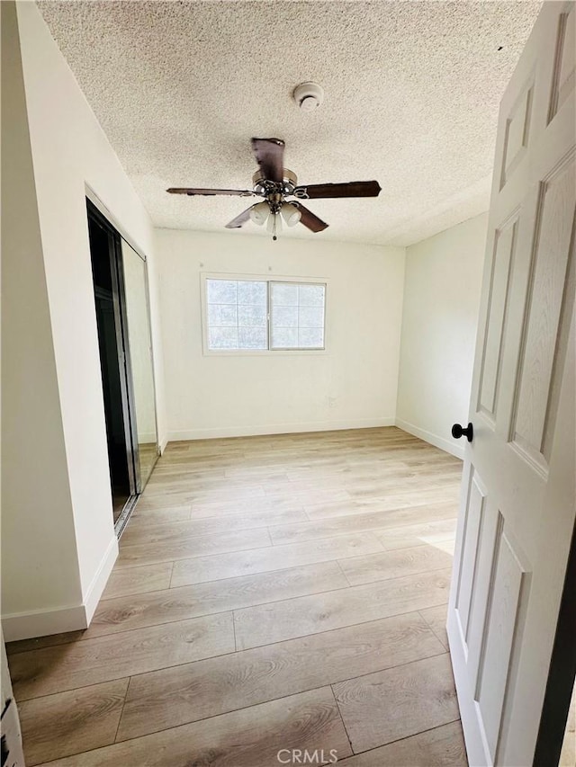 unfurnished bedroom featuring ceiling fan, a closet, light hardwood / wood-style floors, and a textured ceiling