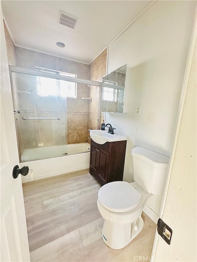 full bathroom with hardwood / wood-style floors, vanity, toilet, and bath / shower combo with glass door