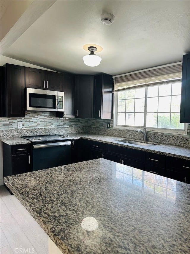 kitchen with light stone countertops, appliances with stainless steel finishes, light wood-type flooring, backsplash, and sink