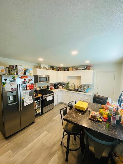 kitchen featuring sink, light hardwood / wood-style flooring, appliances with stainless steel finishes, a textured ceiling, and white cabinets