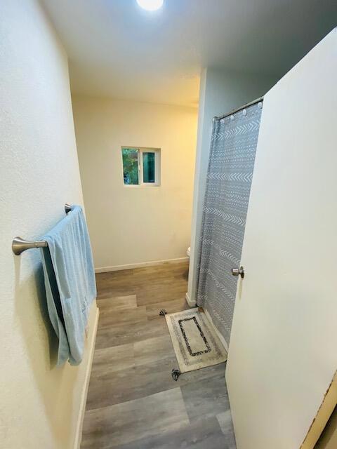 bathroom with toilet, wood-type flooring, and curtained shower