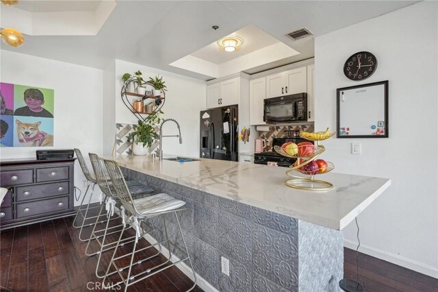 kitchen featuring a breakfast bar, black appliances, kitchen peninsula, sink, and white cabinetry