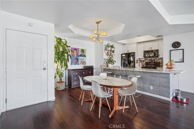 dining room with dark hardwood / wood-style floors, an inviting chandelier, and a tray ceiling