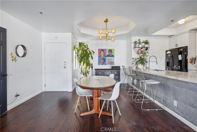 dining area with a raised ceiling, dark hardwood / wood-style flooring, an inviting chandelier, and sink