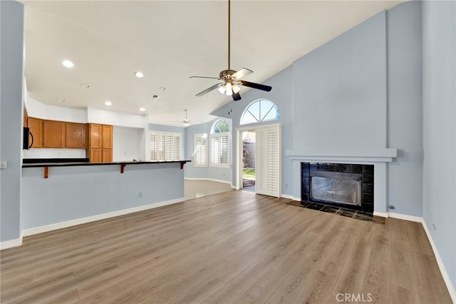 unfurnished living room featuring a tile fireplace, hardwood / wood-style floors, high vaulted ceiling, and ceiling fan