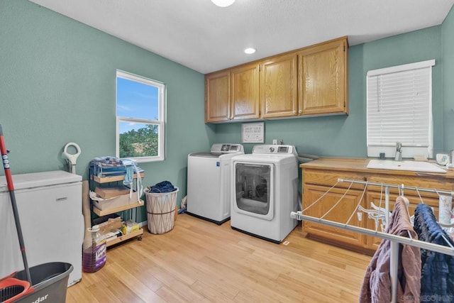 laundry area with washing machine and clothes dryer, light hardwood / wood-style flooring, cabinets, and sink