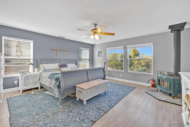 bedroom with a wood stove, ceiling fan, and light wood-type flooring