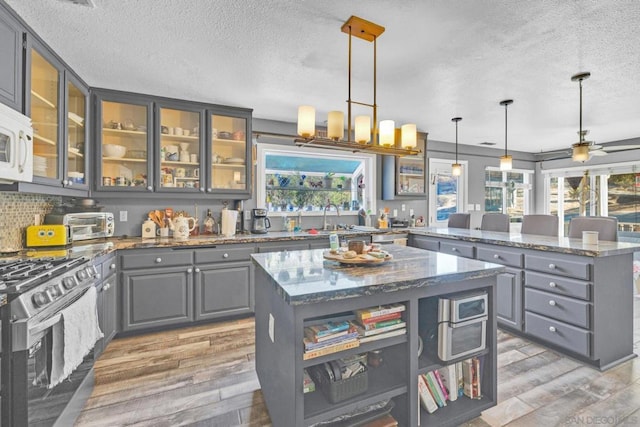 kitchen with light stone countertops, pendant lighting, a center island, and stainless steel gas range