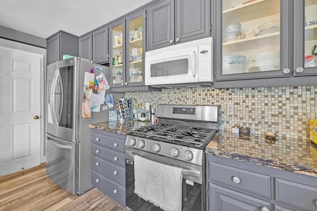 kitchen featuring dark stone counters, hardwood / wood-style flooring, decorative backsplash, gray cabinets, and stainless steel appliances