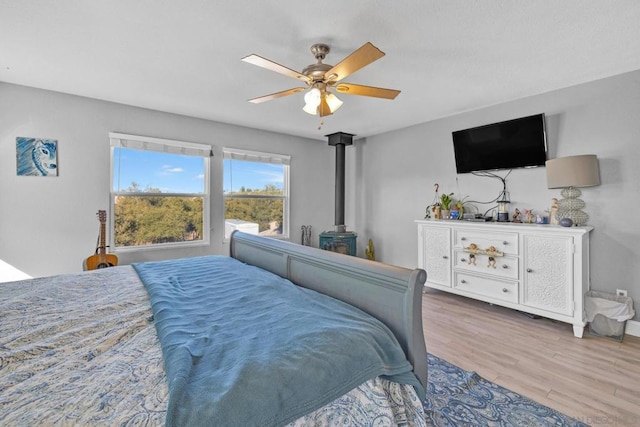 bedroom featuring a wood stove, ceiling fan, and wood-type flooring