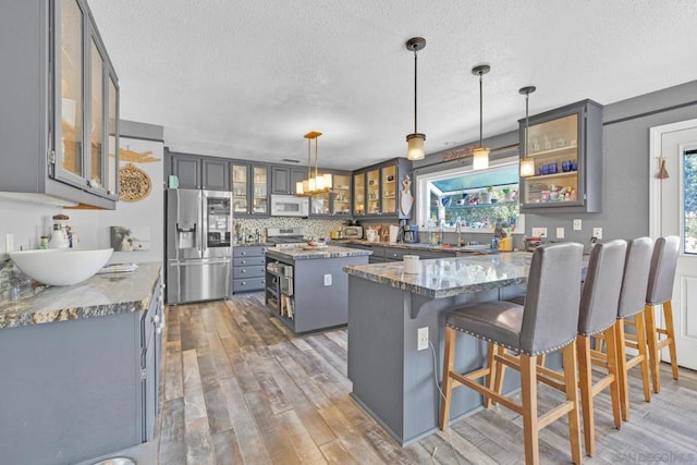 kitchen with a center island, stainless steel fridge with ice dispenser, dark stone counters, pendant lighting, and wood-type flooring