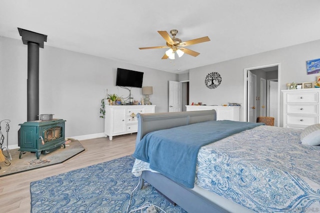 bedroom featuring ceiling fan, a wood stove, and light hardwood / wood-style flooring