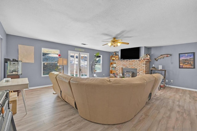 living room with a wood stove, ceiling fan, light hardwood / wood-style flooring, and a textured ceiling