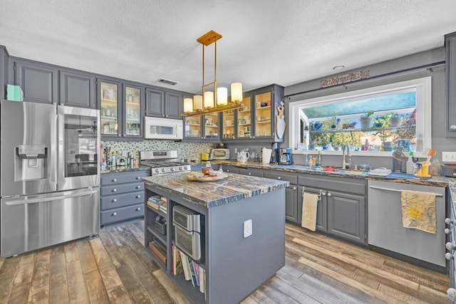 kitchen with dark wood-type flooring, hanging light fixtures, dark stone countertops, appliances with stainless steel finishes, and a kitchen island