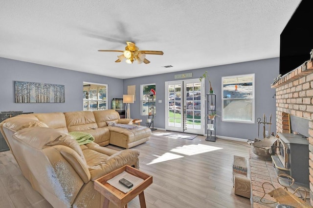 living room featuring a fireplace, ceiling fan, light hardwood / wood-style flooring, and a textured ceiling